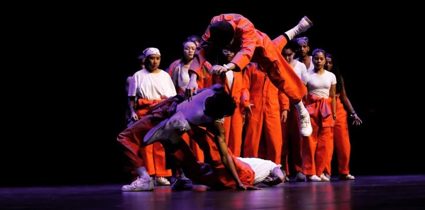 Dance ensemble in orange performing a lift on stage